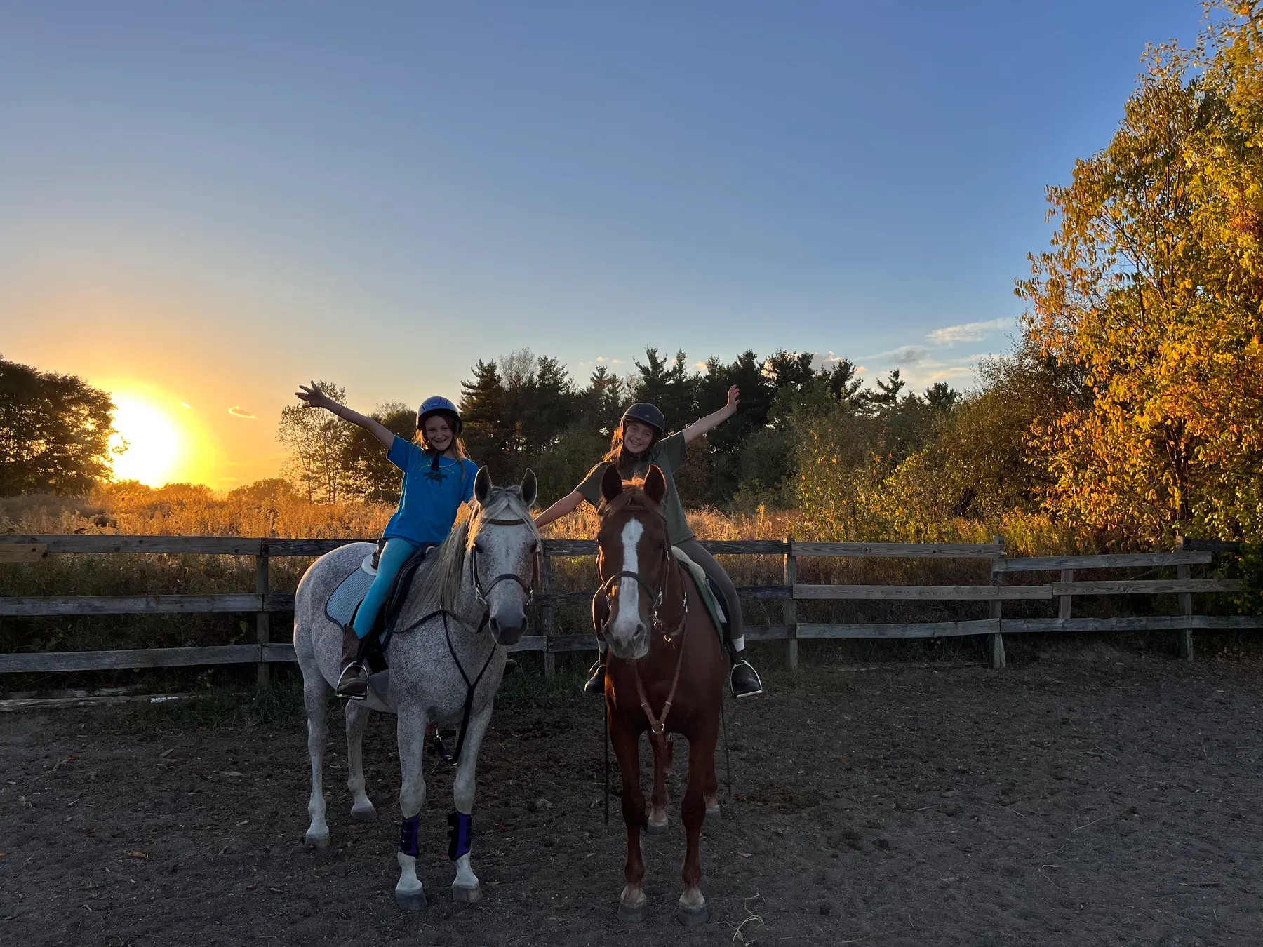 Two young riders smiling on horseback at sunset at MSB Riding Academy